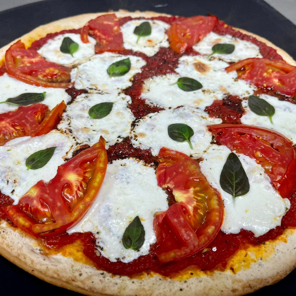 A freshly baked Lion's Den Pizzeria pizza with sliced tomatoes, mozzarella, and basil leaves.
