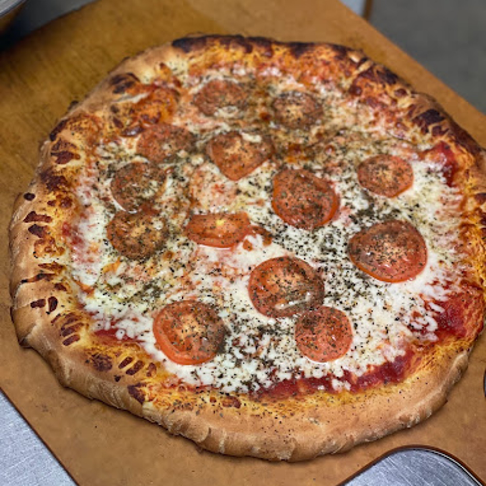 A freshly baked Lion's Den Pizzeria pizza with sliced tomatoes, mozzarella, and herbs.