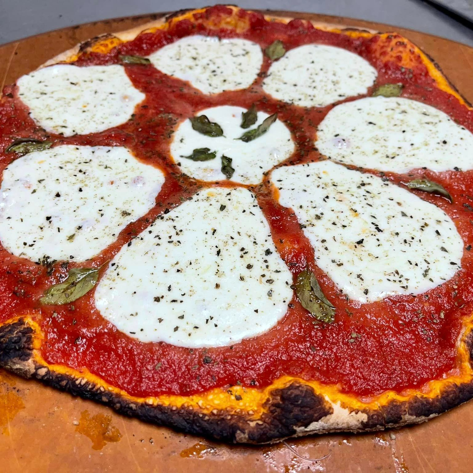 A Lion's Den Pizzeria pizza with fresh mozzarella, red sauce, and basil on a wooden peel.
