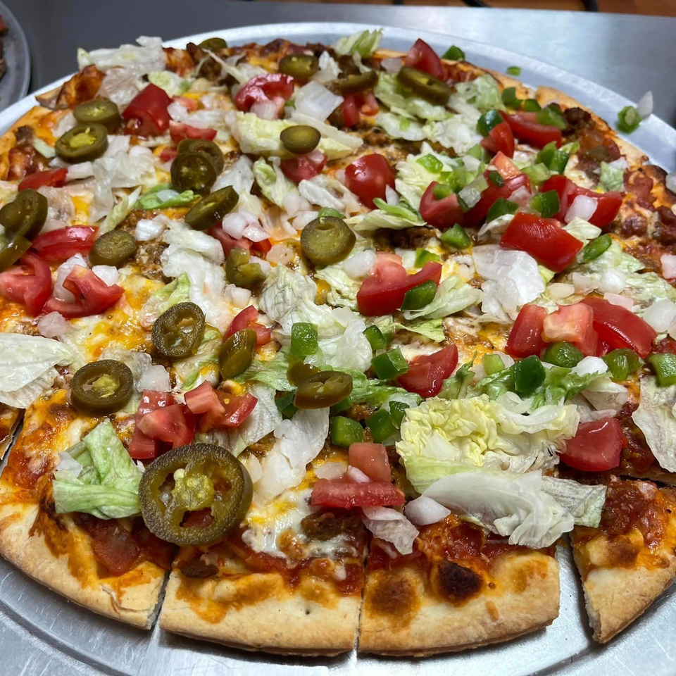 A Lion's Den Pizzeria taco pizza, topped with lettuce, tomatoes, onions, and jalapeños.