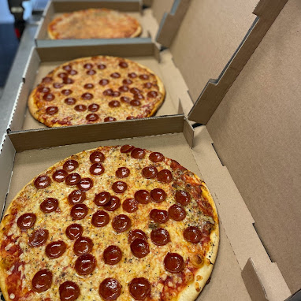Three pepperoni pizzas in open cardboard boxes, ready for delivery from Lion's Den Pizzeria.