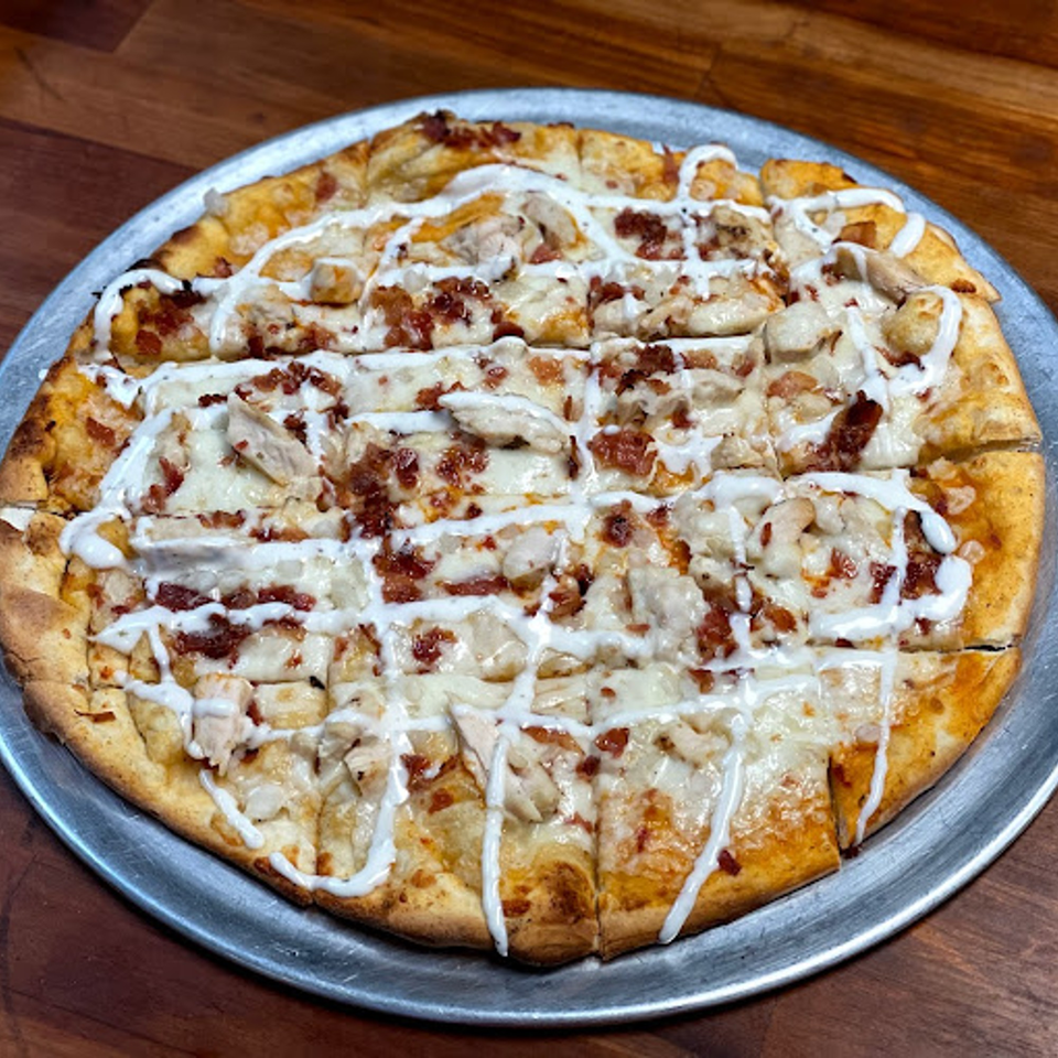 A Lion's Den Pizzeria chicken bacon ranch pizza, cut into squares, on a metal pan.
