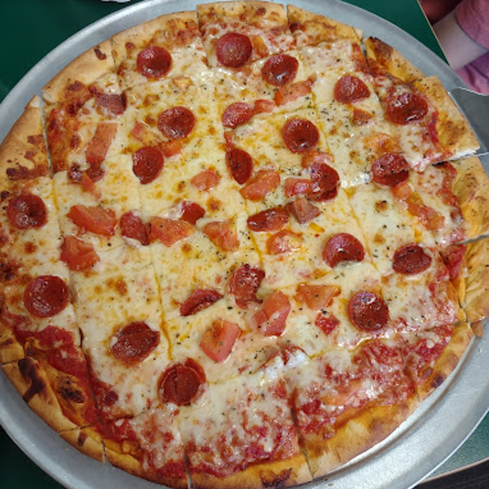 A whole Lion's Den Pizzeria pepperoni and tomato pizza on a metal tray.