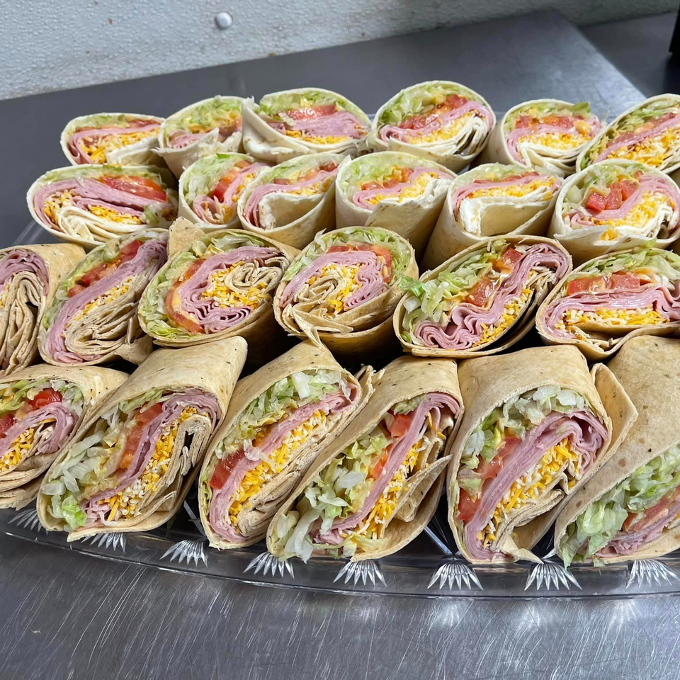 A platter of many ham and cheese wraps with lettuce and tomato, cut in half.