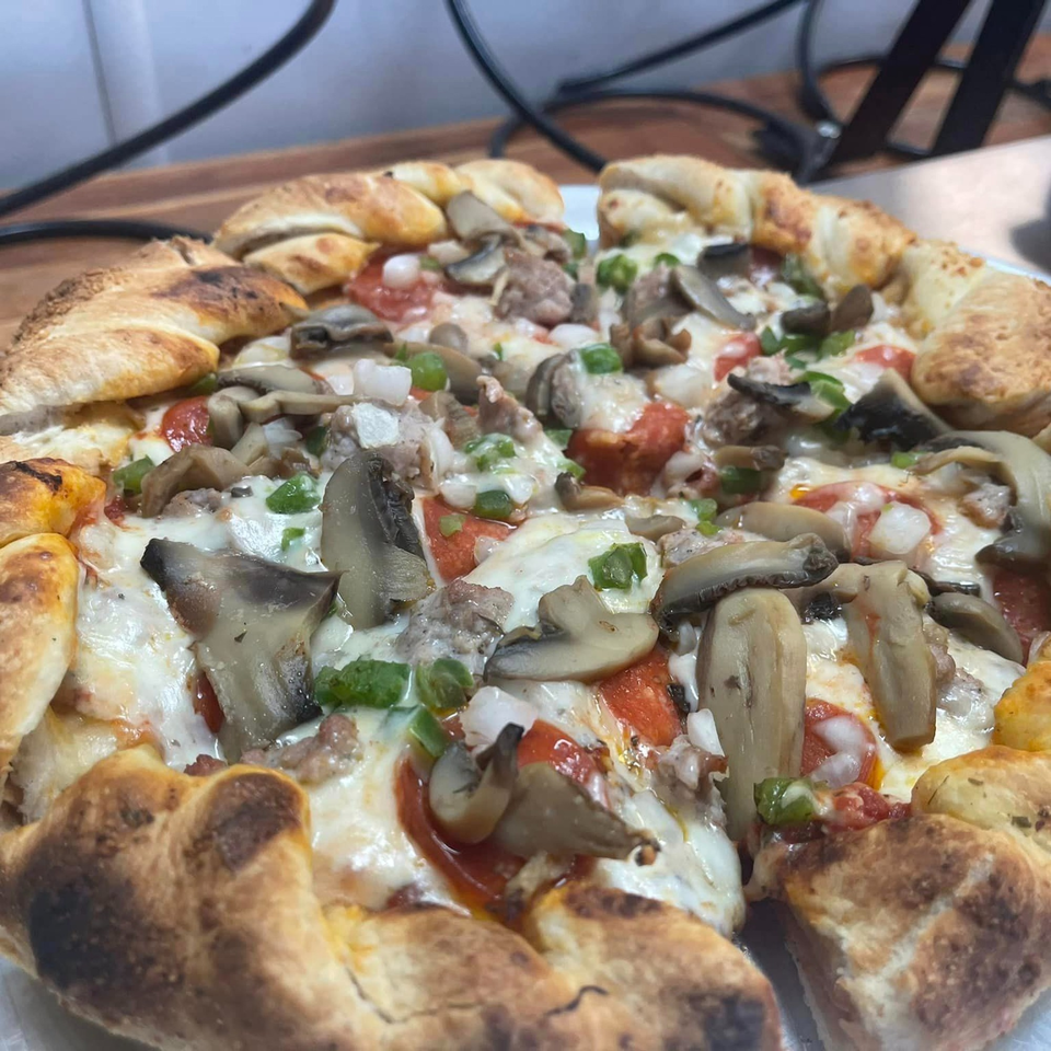 Close-up of a Lion's Den Pizzeria pizza with mushrooms, sausage, and green peppers.
