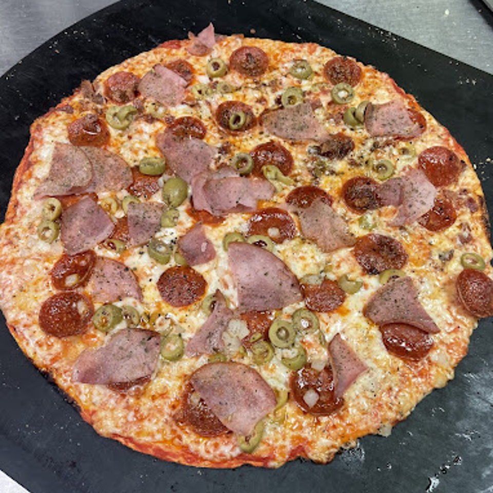 A freshly baked Lion's Den Pizzeria pizza, topped with pepperoni, ham, and green olives.