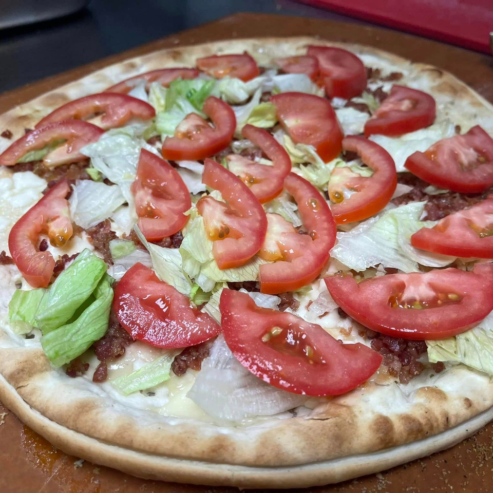 A freshly baked Lion's Den Pizzeria pizza topped with lettuce, tomatoes, and bacon.