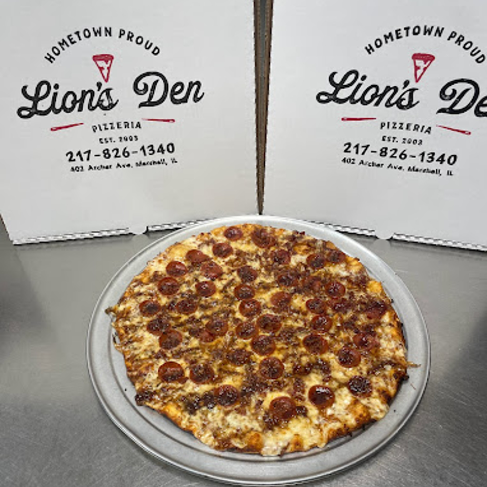 A Lion's Den Pizzeria pepperoni and sausage pizza on a metal tray with two pizza boxes behind it.