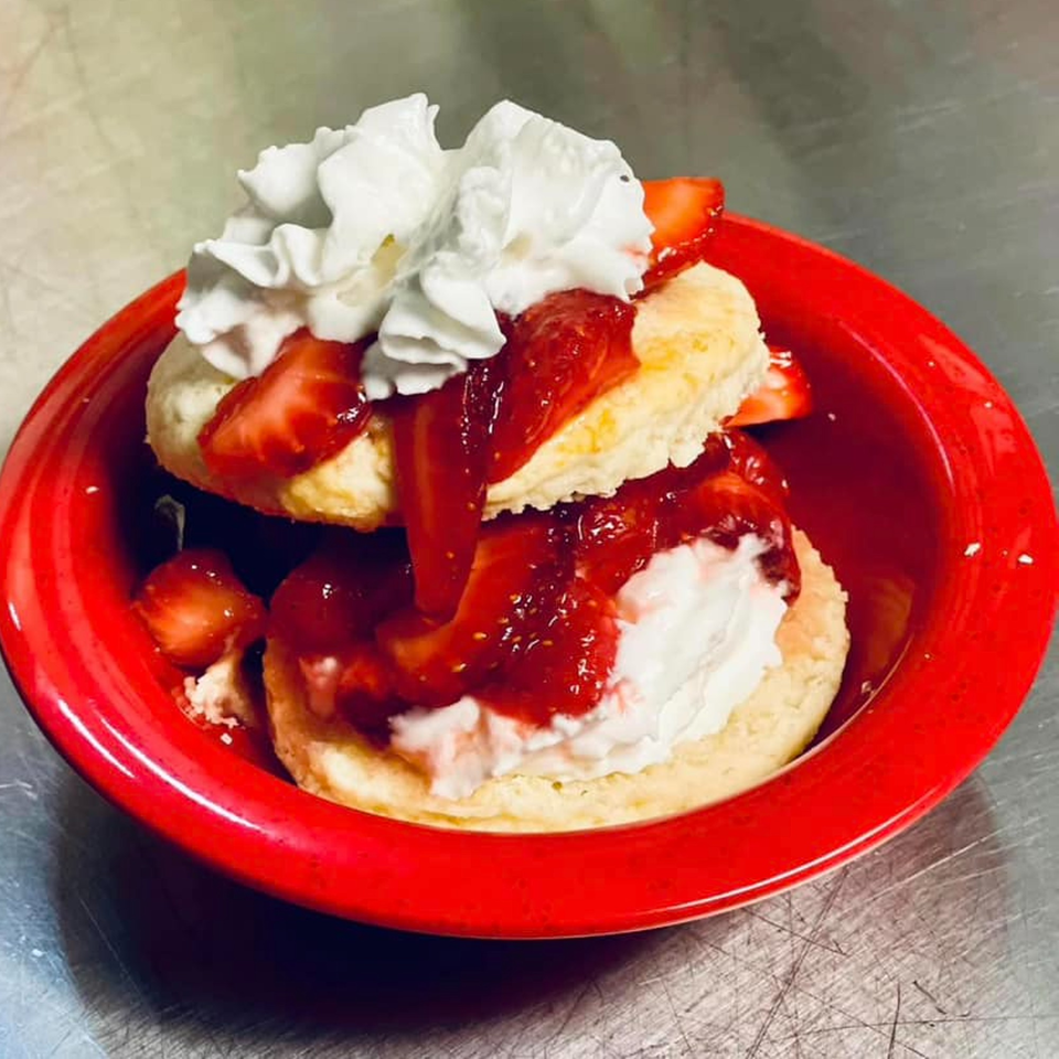 Strawberry shortcake with whipped cream and strawberry sauce in a red bowl.