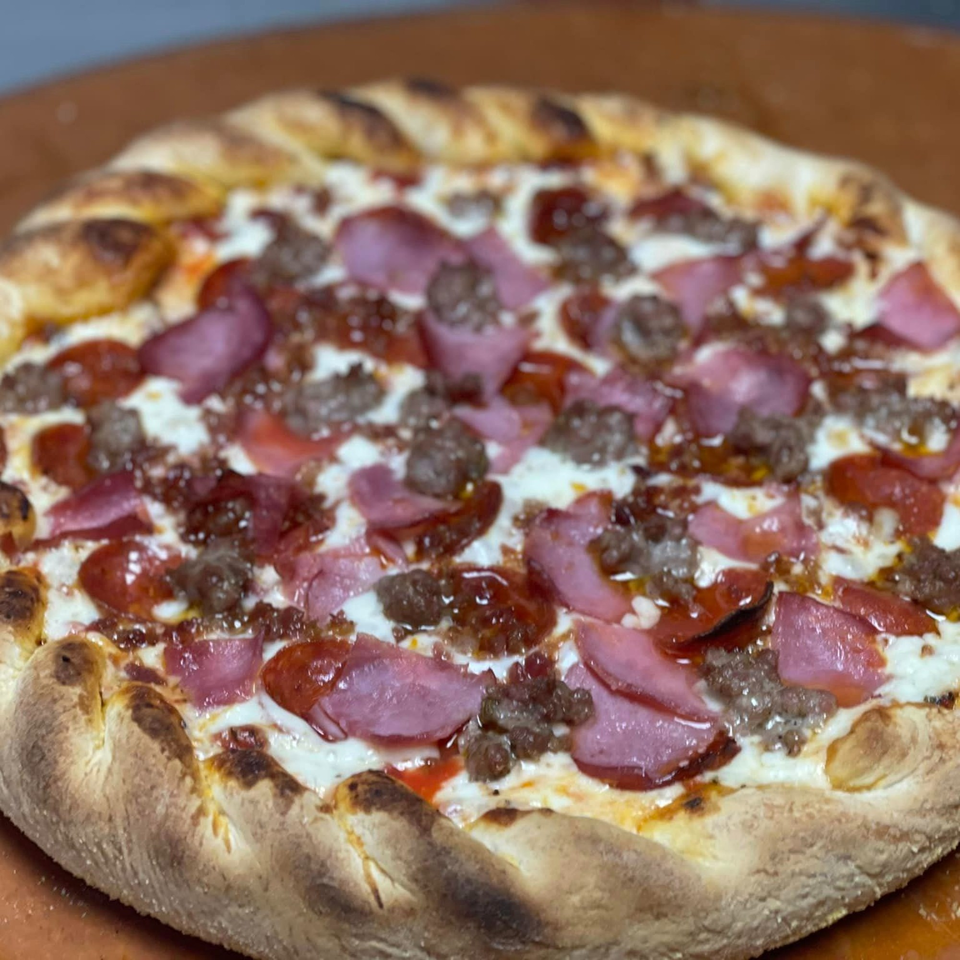 A freshly baked Lion's Den Pizzeria pizza, topped with pepperoni, sausage, and ham.