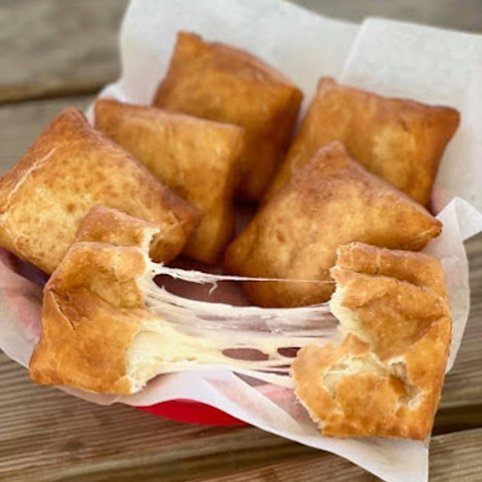 Golden-brown fried dough squares, one pulled apart to reveal stretchy melted mozzarella cheese inside.