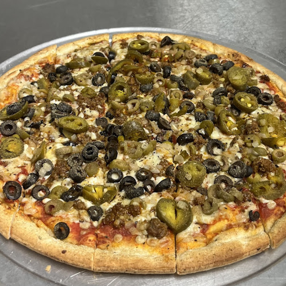 Lion's Den Pizzeria's pizza with ground meat, black olives, and jalapeños on a metal tray.